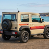 Beige Suzuki Jimny with red stripes from a rear three-quarter perspective beside the coast