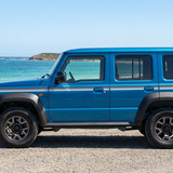 Blue five-door Jimny with grey and blue stripes beside an Australian beach and turquoise ocean