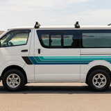 White HiAce with navy and teal stripes beside the coast